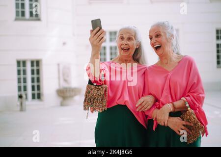 Senior women twins outdoors in city taking selfie. Stock Photo