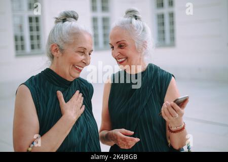 Happy senior twins in same clothes talking and walking in city. Stock Photo