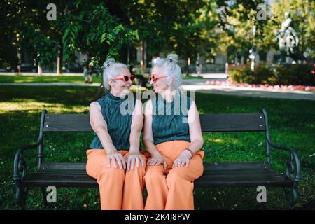 Happy senior sister, twins sitting in city park and resting after shopping. Stock Photo