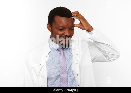 Confused black doctor man with small beard in white robe bright shirt isolated on white background. Forgetful black african american physician therapi Stock Photo