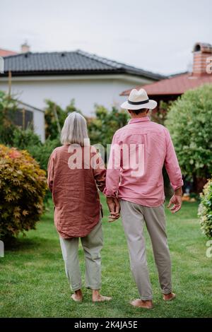 Rear view of senior couple posing together in their garden, holding each other hands. Stock Photo