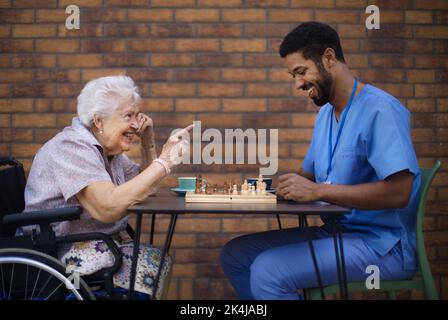 Caregiver playing chess and drinking coffe with his client outdoor at a cafe. Stock Photo