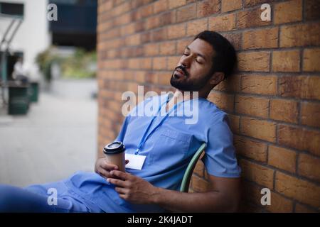 Tired caregiver man resting outdoor, in front of nurishing home. Stock Photo
