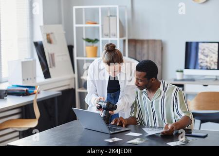 Portrait of two young photographers working with pictures and using laptop in studio Stock Photo