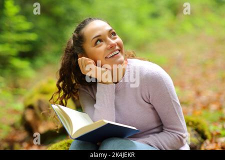 Happy woman dreaming while read a book in a forest looking above Stock Photo
