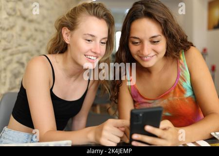 Two happy friends checking phone together in a restaurant Stock Photo