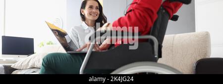 Friends spend time together watching movie on laptop, disabled woman in wheelchair Stock Photo