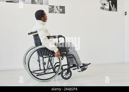 Black young man using wheelchair while visiting modern art gallery, copy space Stock Photo