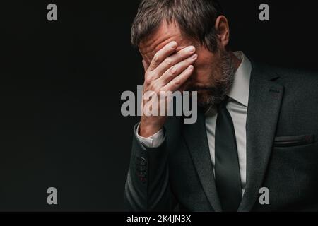Business failure, disappointed businessman covering face in disbelief after bankruptcy, low key portrait with copy space and selective focus Stock Photo