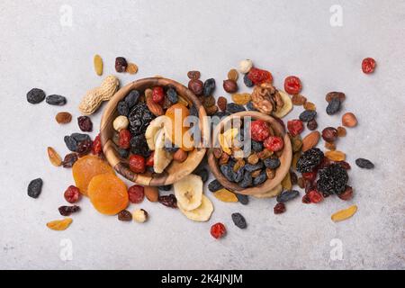 Top view of wooden bowls with dried fruit, berries and nuts as ingredient for tasty and healthy meal on grey concrete background Stock Photo