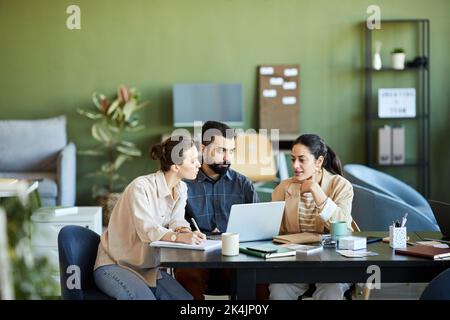 Young woman sharing her ideas or viewpoint with colleagues during work over new business project by workplace in front of laptop Stock Photo