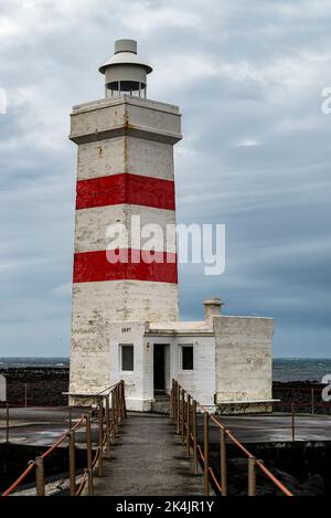 The old Garðskagi lighthouse in Garður under a cloudy sky, Reykjanes Peninsula, Iceland. Built in 1897, the lighthouse is about 12.5 meters high. Stock Photo