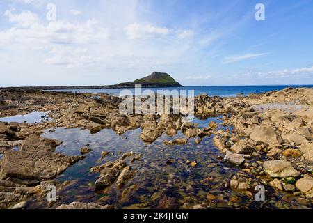 Shallow rock pools and jagged rocks covered with mussels and limpets on the causeway to Worms Head. Stock Photo