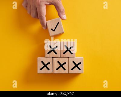 Hand putting wooden cube with tick checkmark right icon over the cross wrong icons. Finding the correct way after making many mistakes. Stock Photo