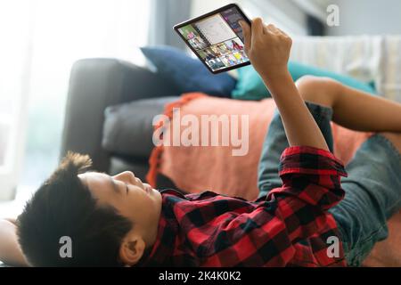 Smiling asian boy using tablet for video call, with diverse elementary school pupils on screen. communication technology and online education, digital Stock Photo