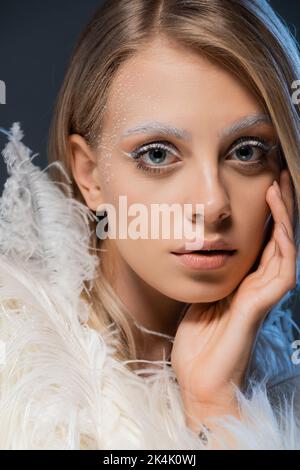 portrait of young woman in faux fur jacket posing with white feather isolated on dark blue,stock image Stock Photo