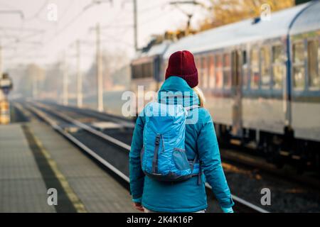 Woman looking at leaving train on railroad station. Female backpacker travel by train alone Stock Photo