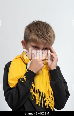 A child blows his nose into a napkin, children's seasonal diseases, a boy wrapped in a scarf. Stock Photo