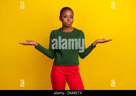 Photo of doubtful pretty young woman wear green shirt shrugging shoulders arms empty space isolated yellow color background Stock Photo