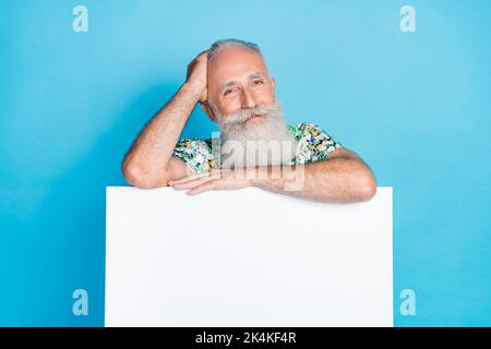 Photo of positive aged man behind empty space ad billboard isolated on blue color background Stock Photo