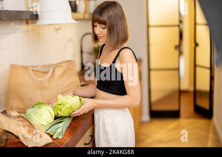 Woman unpacks freshly bought vegetables on kitchen table Stock Photo