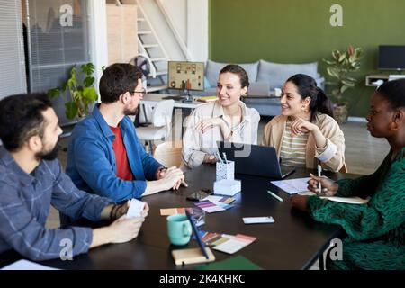 Group of young intercultural designers gathered by table brainstorming and having discussion of ideas for their new project at meeting Stock Photo