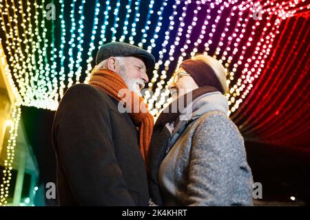 Elderly couple in romantic embrace under the colorful Christmas lights Stock Photo