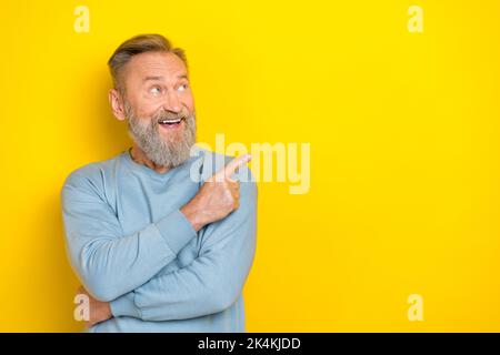 Photo of funny excited man pensioner dressed blue pullover looking pointing finger empty space isolated yellow color background Stock Photo