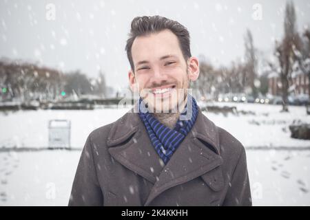 Portrait of young handsome man with beard smiling laughing looking at camera in winter snow Stock Photo