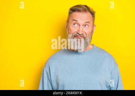Photo of suspicious funny man pensioner dressed blue pullover looking empty space isolated yellow color background Stock Photo