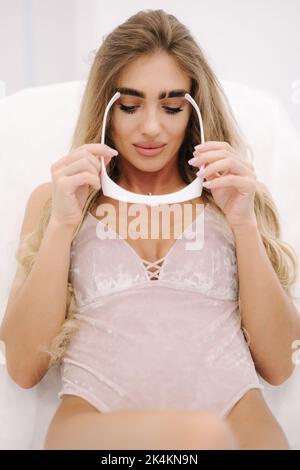 Beautiful model wears protective glasses before starting laser light hair removal. Treatment for hairless smooth skin at cosmetology salon Stock Photo