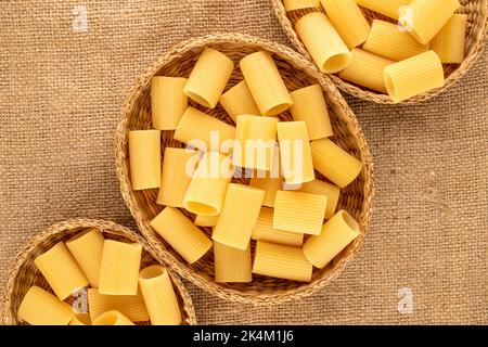 Several blue yellow cannelloni in straw plates on jute cloth, macro, top view. Stock Photo