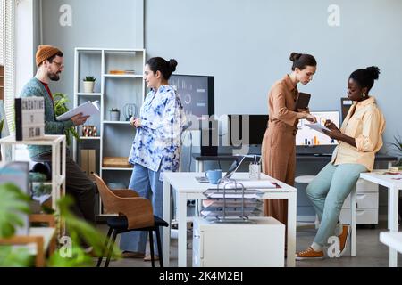 Two small group of young successful coworkers in casualwear discussing their ideas and notes while preparing for seminar in office Stock Photo
