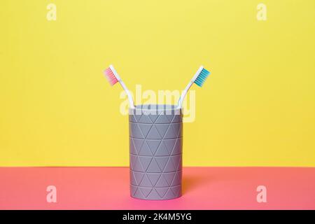 Two toothbrushes stand with a gray glass on a yellow background. Toothbrush concept for a couple, living together as the beginning of a family Stock Photo