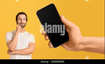 Pensive millennial european man look at huge smartphone with blank screen in hand Stock Photo