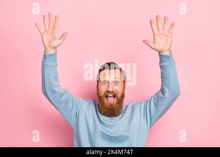 Photo of impressed overjoyed cheerful guy with ginger beard dressed blue sweater scream yes hands up isolated on pink color background Stock Photo