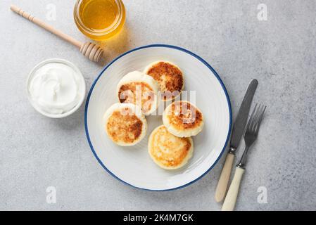 Syrniki, sweet curd cheese or ricotta cheese fritters on white plate, grey concrete background, top view Stock Photo