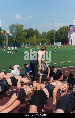 Female coach and group of children conducts a training session at the stadium. School gym trainings or athletics Stock Photo