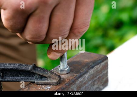 A man's hand screws a bolt into a metal nut. Working with metal Stock Photo