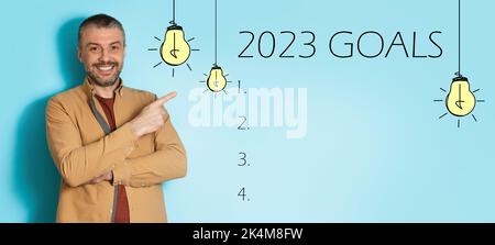 Happy adult european man point finger at inscription goals 2023 with light bulbs, checklist with copy space Stock Photo