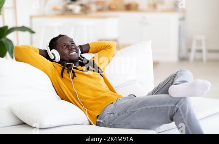 Smiling Young Black Guy Wearing Headphones Relaxing On Couch In Living Room Stock Photo