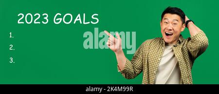 Cheerful shocked adult asian man point finger at 2023 goals with light bulbs, checklist with free space Stock Photo