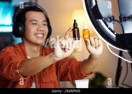 Selective focus shot of modern young Asian male beauty blogger sitting making promotion video for new skincare products Stock Photo