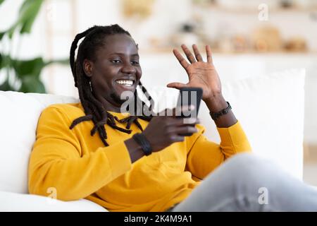 Distant Communication. Smiling Black Guy Making Video Call Via Smartphone At Home Stock Photo