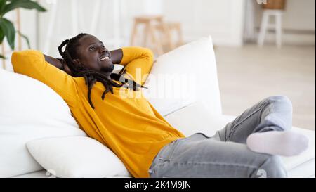 Relaxing Weekend. Happy Smiling Young Black Man Leaning Back On Couch Stock Photo
