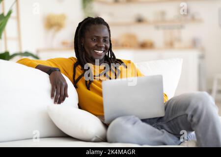 Handsome Black Guy With Dreadlocks Relaxing With Laptop On Couch At Home Stock Photo