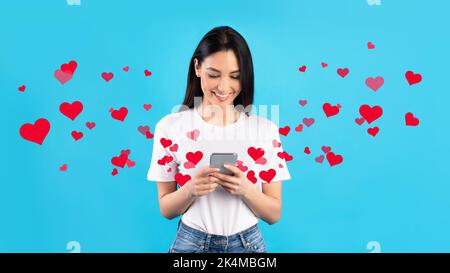 Happy young woman using smartphone, sending love message Stock Photo