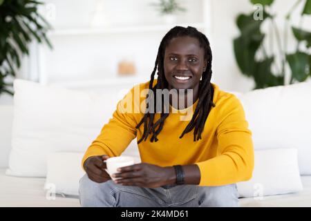 Handsome Young Black Man Drinking Coffee While Relaxing On Couch At Home Stock Photo