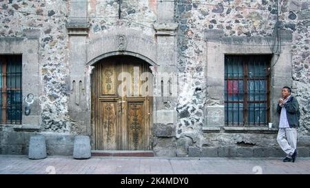 man eating on the facade of a building with wood and stone door, mexico Stock Photo
