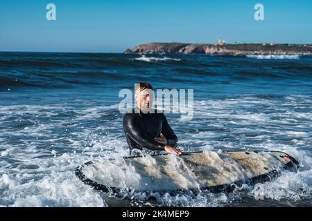 Man holding his surfboard on the shore, while fighting against the current of the sea. Stock Photo